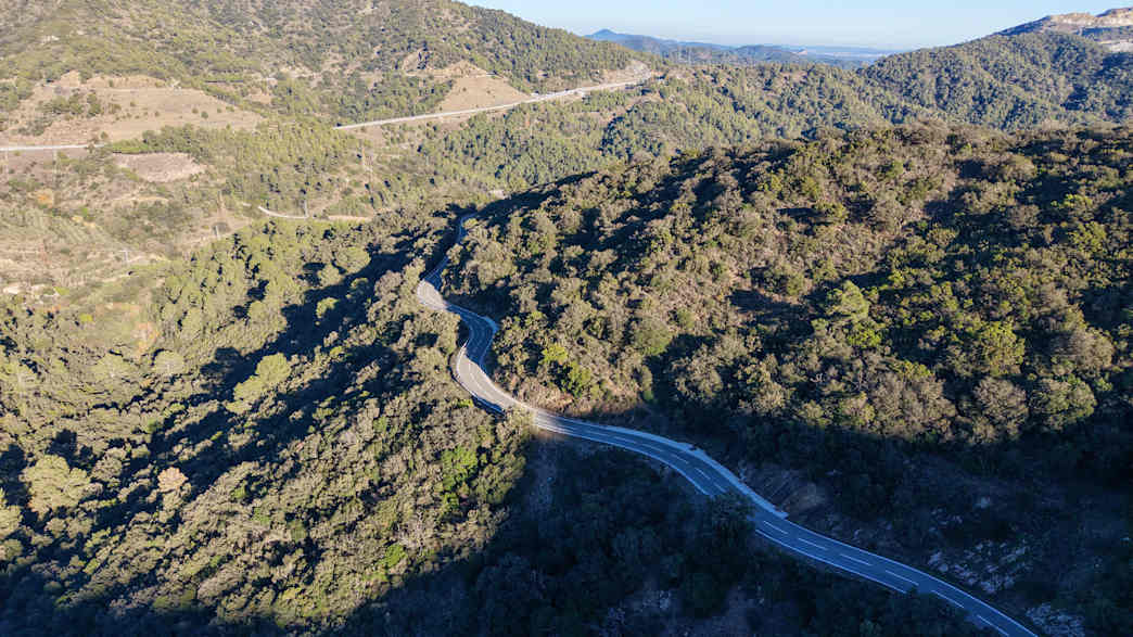 Kurvige Straße durch das trockene Hinterland von Tarragona, umgeben von Hügeln und mediterraner Buschlandschaft.