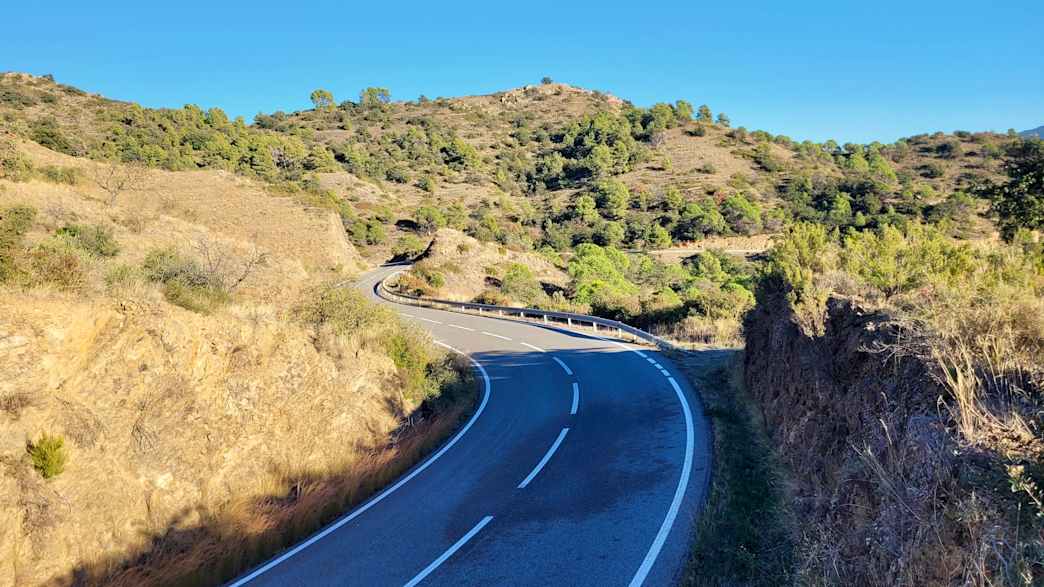 Kurvige Straße nahe Tarragona, eingebettet in trockene Hügel und gelbgrüne Vegetation, klare Sicht und sonnige Bedingungen.